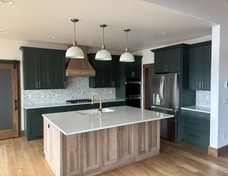 Open kitchen with quartzite countertops and custom green cabinets with gold hardware and marble backsplash.